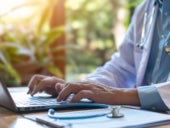 A doctor typing on a laptop keyboard, updating patient medical records for consulting.