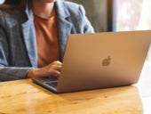 A woman using and working on Apple MacBook Pro laptop computer on wooden table.